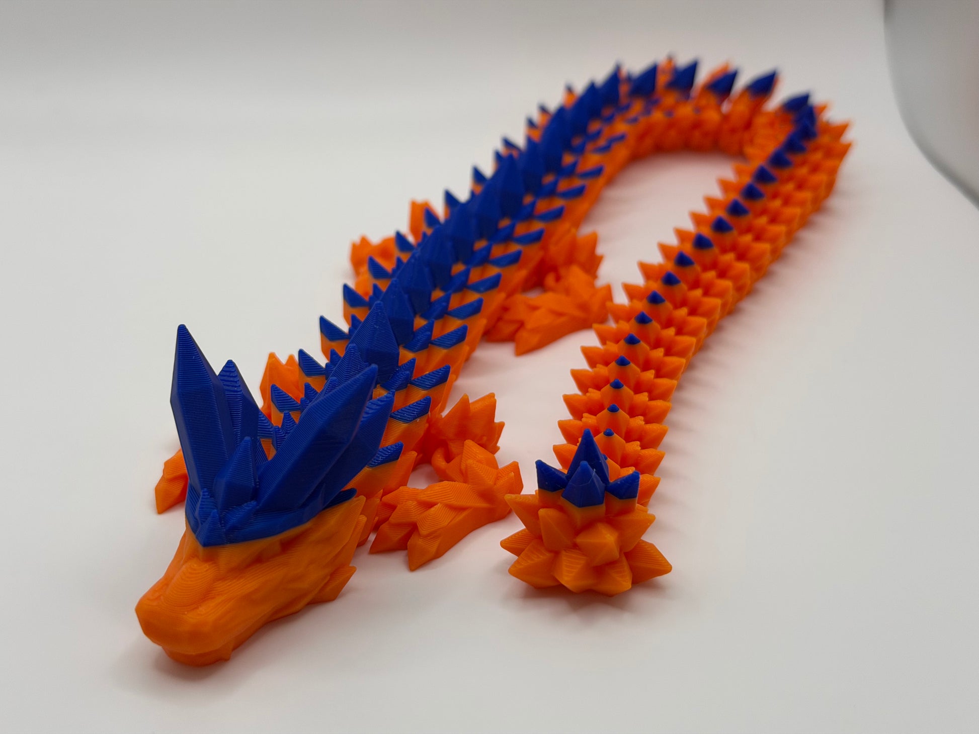 A fully articulated 18-inch 3D printed Crystal Dragon figure in vibrant blue and orange PLA, featuring crystal-shaped spikes and a segmented, poseable body.