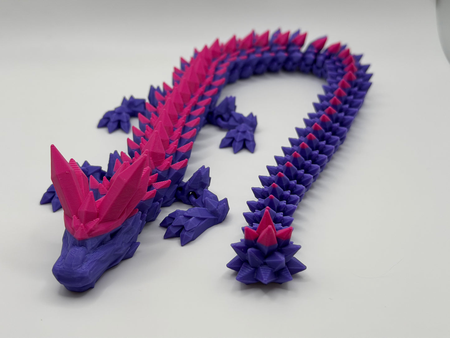 A fully articulated 18-inch 3D printed Crystal Dragon figure in pink and purple PLA, featuring crystal-shaped spikes and a segmented, poseable body.