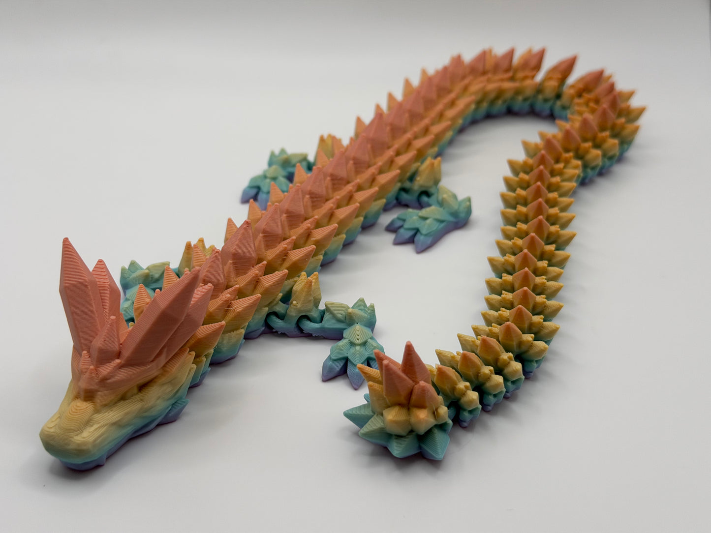 A fully articulated 18-inch 3D printed Crystal Dragon figure in rainbow colored PLA, featuring crystal-shaped spikes and a segmented, poseable body.