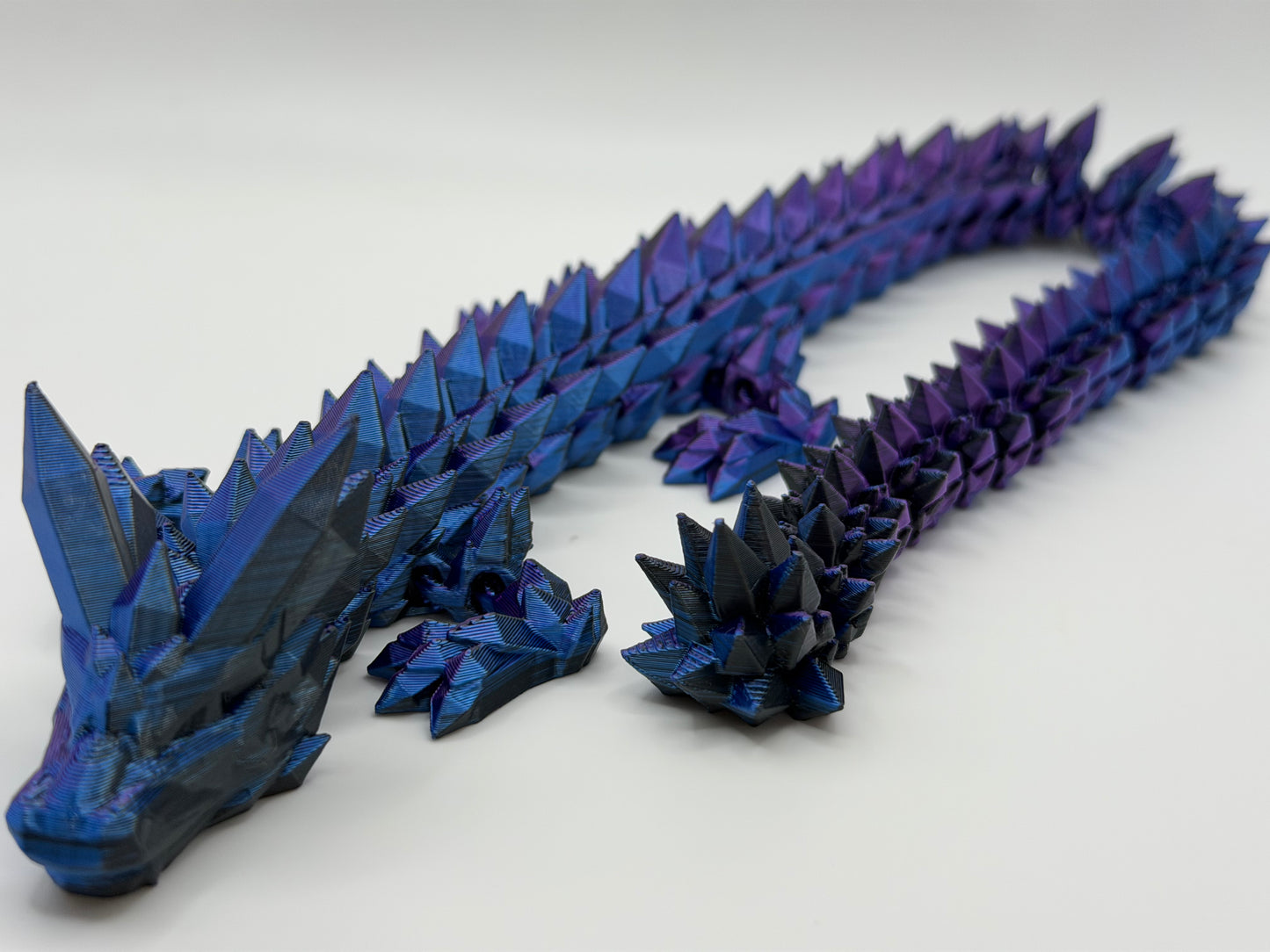 A fully articulated 18-inch 3D printed Crystal Dragon figure in blue/purple silk PLA, featuring crystal-shaped spikes and a segmented, poseable body.