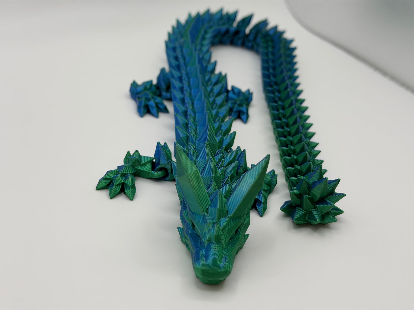 A fully articulated 18-inch 3D printed Crystal Dragon figure in blue/green silk PLA, featuring crystal-shaped spikes and a segmented, poseable body.