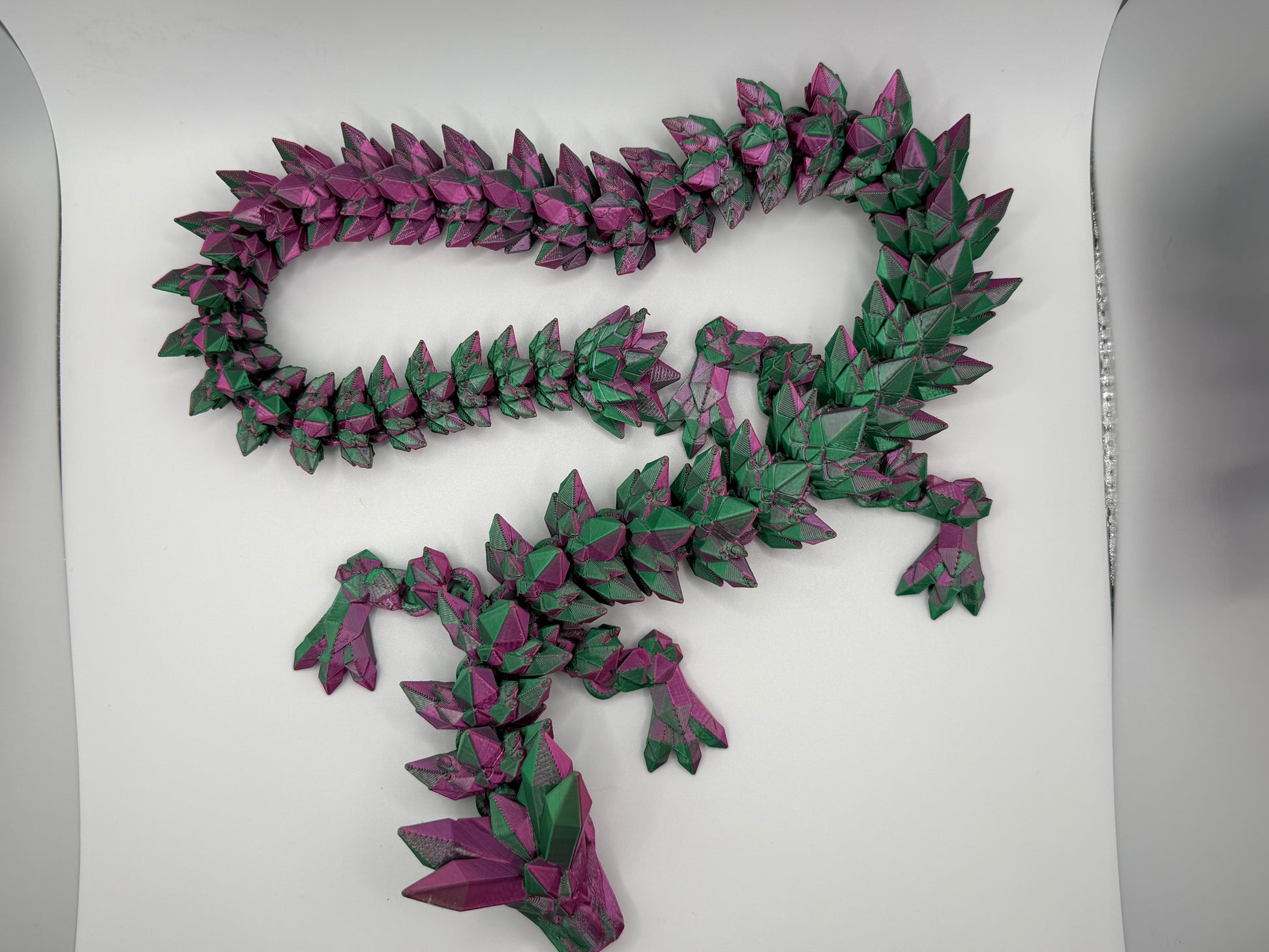 A fully articulated 26-inch 3D printed Crystal Dragon figure in purple/green silk PLA, featuring crystal-shaped spikes and a segmented, poseable body.