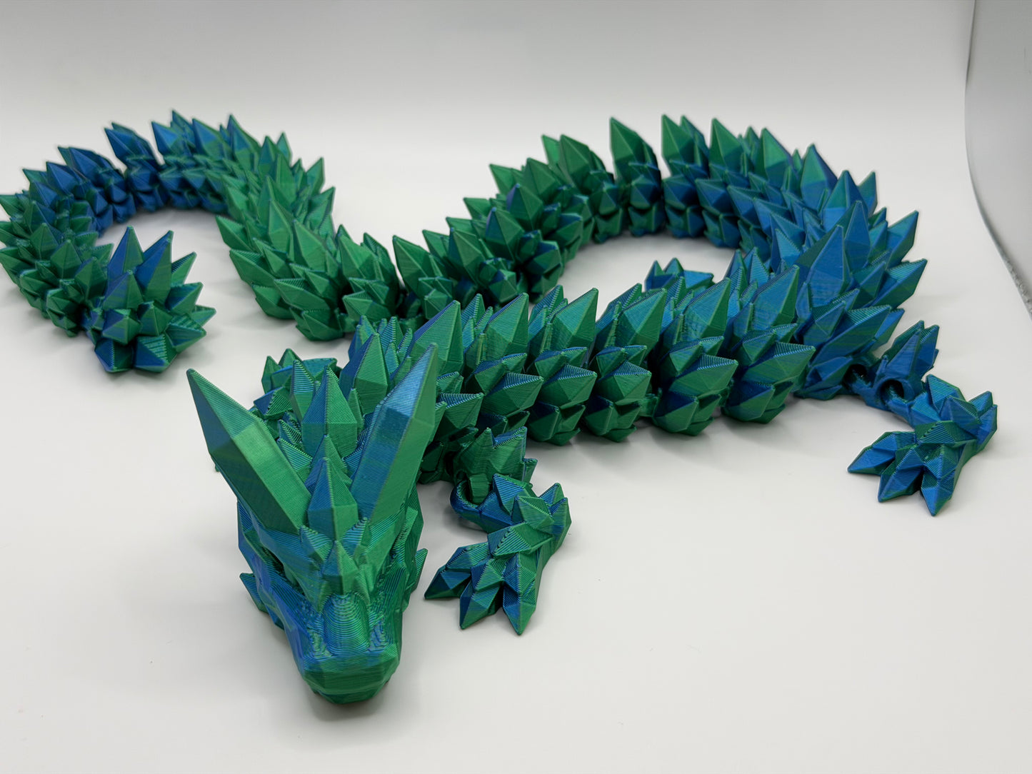 A fully articulated 26-inch 3D printed Crystal Dragon figure in blue/green silk PLA, featuring crystal-shaped spikes and a segmented, poseable body.