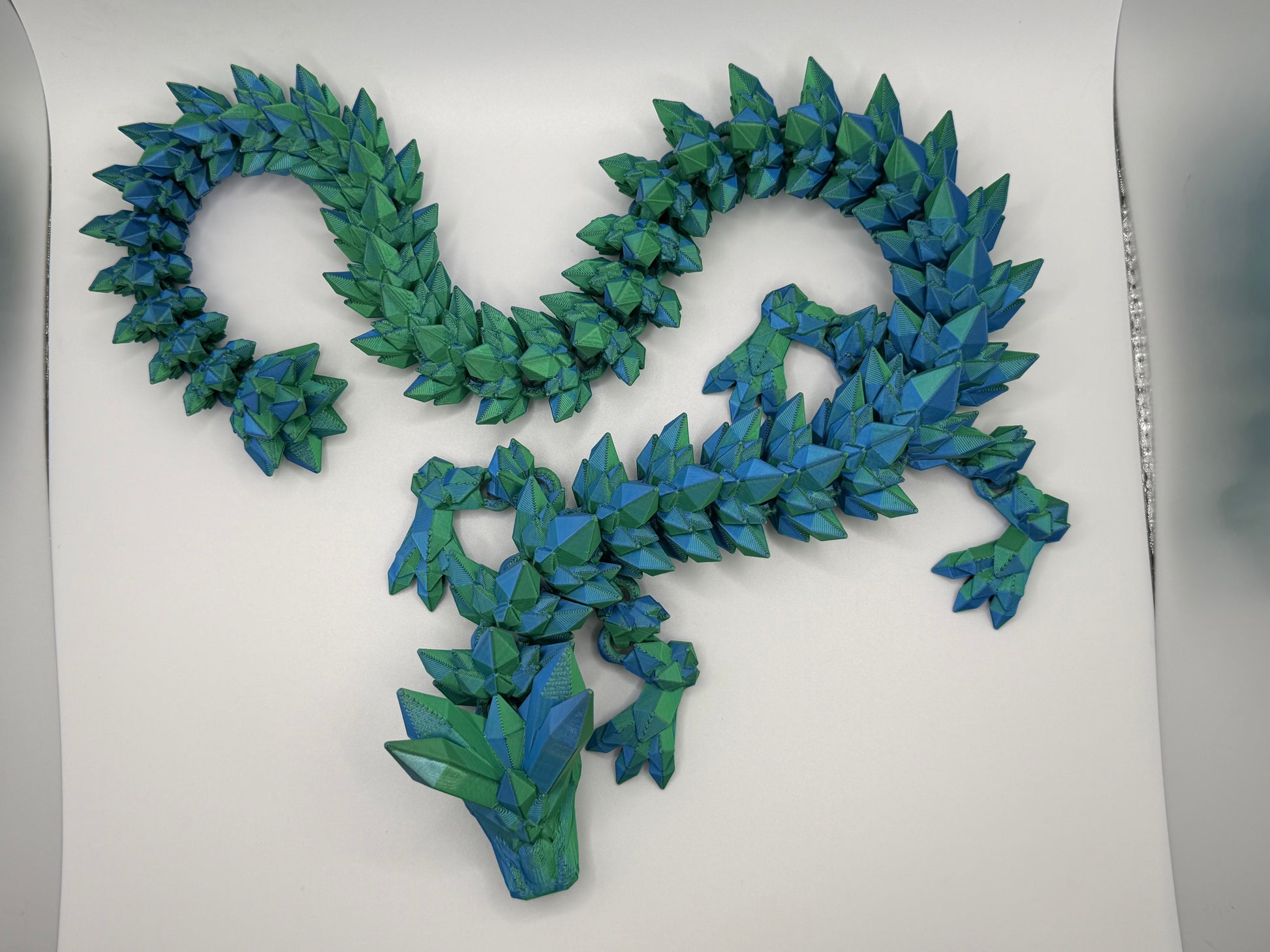 A fully articulated 26-inch 3D printed Crystal Dragon figure in blue/green silk PLA, featuring crystal-shaped spikes and a segmented, poseable body.