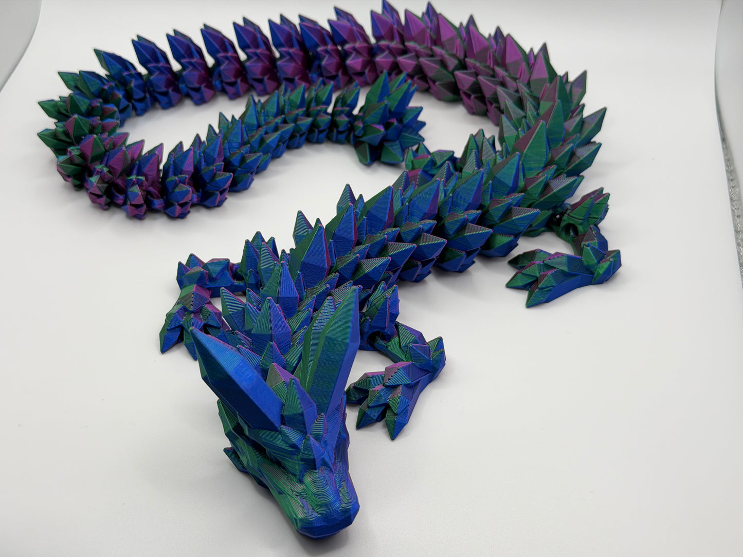 A fully articulated 26-inch 3D printed Crystal Dragon figure in blue/purple/green silk PLA, featuring crystal-shaped spikes and a segmented, poseable body.
