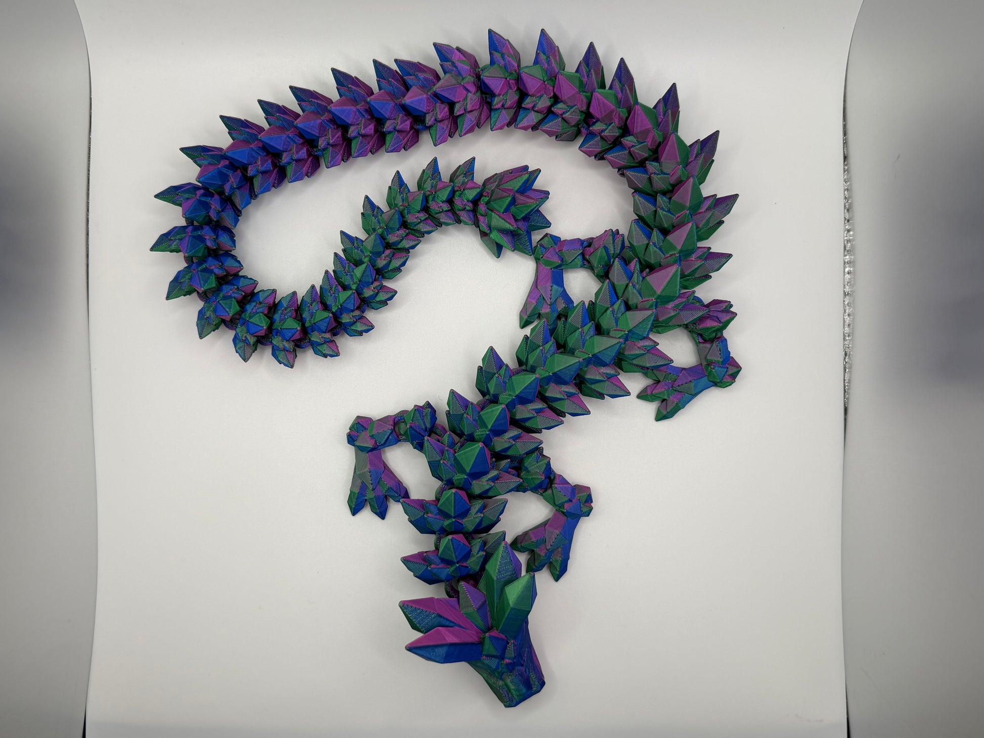 A fully articulated 26-inch 3D printed Crystal Dragon figure in blue/purple/green silk PLA, featuring crystal-shaped spikes and a segmented, poseable body.