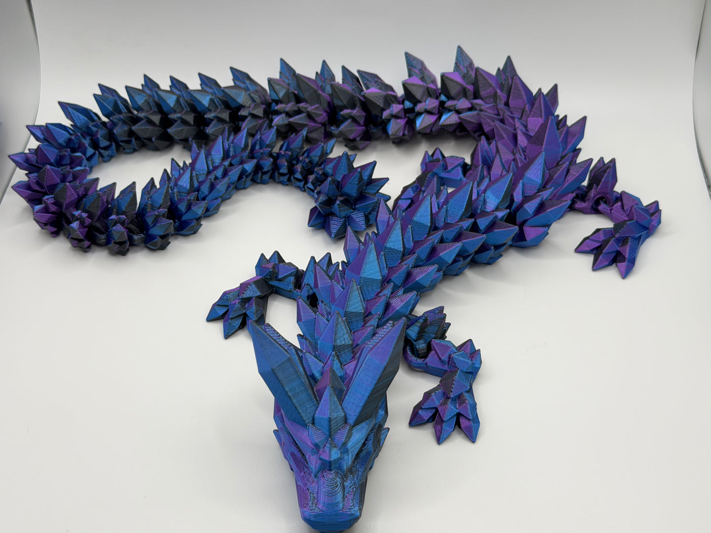 A fully articulated 26-inch 3D printed Crystal Dragon figure in blue/purple/black silk PLA, featuring crystal-shaped spikes and a segmented, poseable body.
