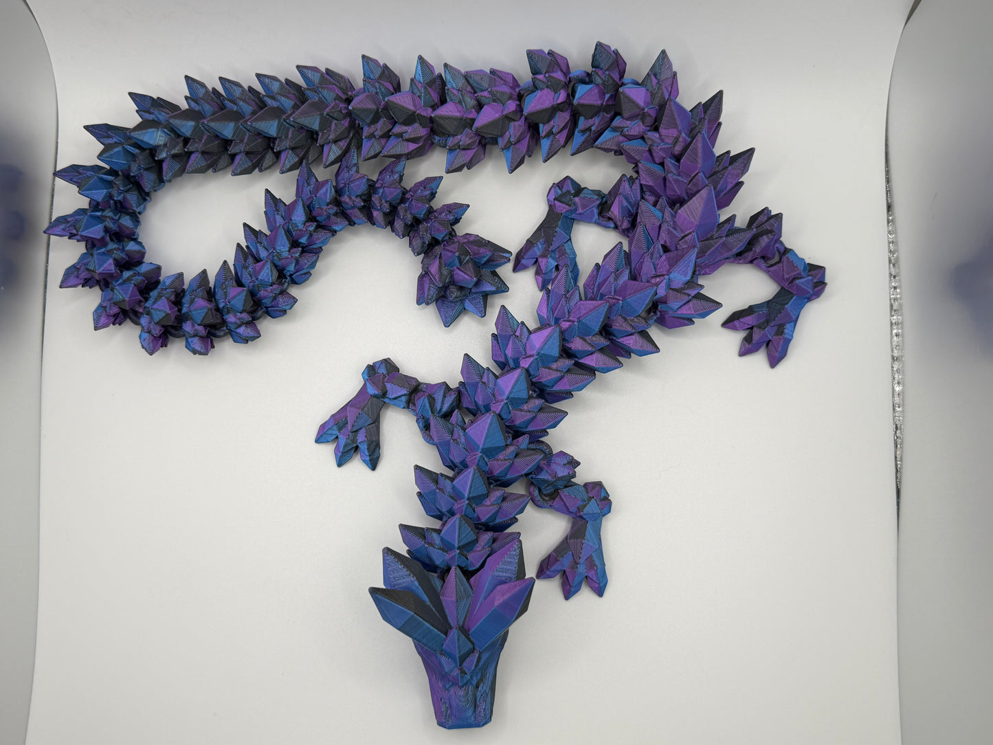 A fully articulated 26-inch 3D printed Crystal Dragon figure in blue/purple/black silk PLA, featuring crystal-shaped spikes and a segmented, poseable body.